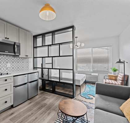 A modern kitchen with a grey couch and a wooden table.