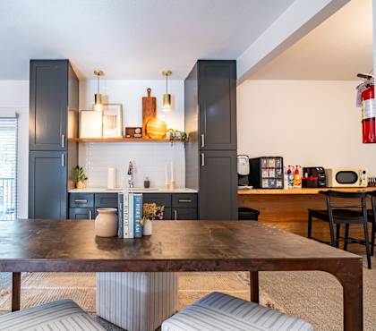 a living room with a wooden table and a kitchen with grey cabinets