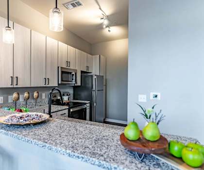 A kitchen with granite countertops and a tray of green apples.