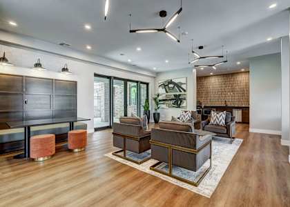 Westlake Greens' lounge features four armchairs, pendant lighting, artwork, a dark table with stools, and a textured brick wall.