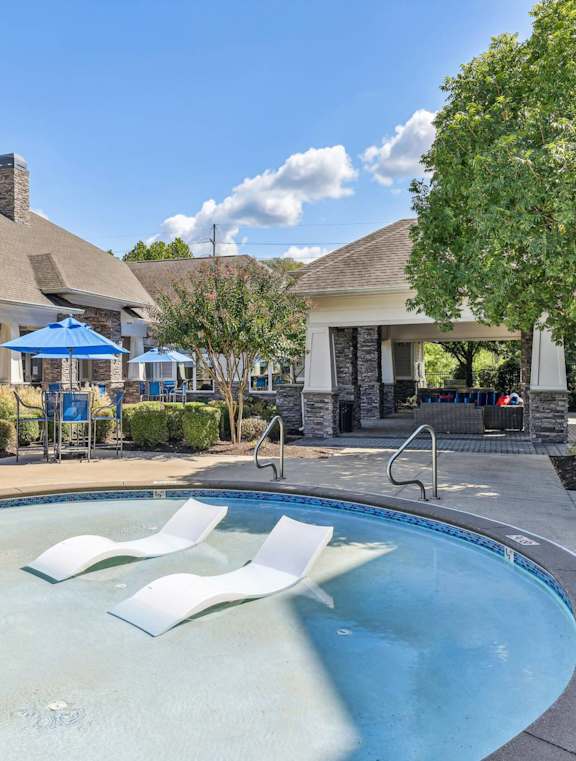 A swimming pool with a blue umbrella and lounge chairs.