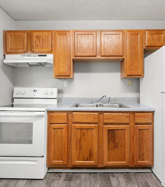 A kitchen with white appliances and wooden cabinets at Balfour Forest Apartments in GA, 30008