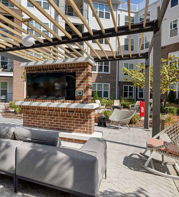 A patio with a couch and a television under a wooden roof.