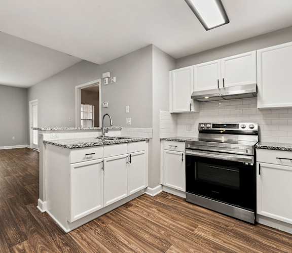 A kitchen with white cabinets and a wooden floor at Crogman School Lofts in Georgia 30315
