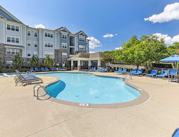 A large swimming pool surrounded by blue lounge chairs and a building in the background.
