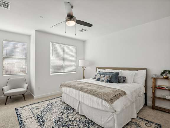 A bedroom with a large bed, a chair, and a ceiling fan.