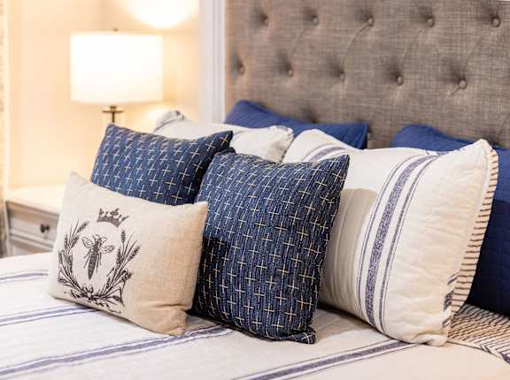 A bed with blue and white pillows and a lamp in the background.