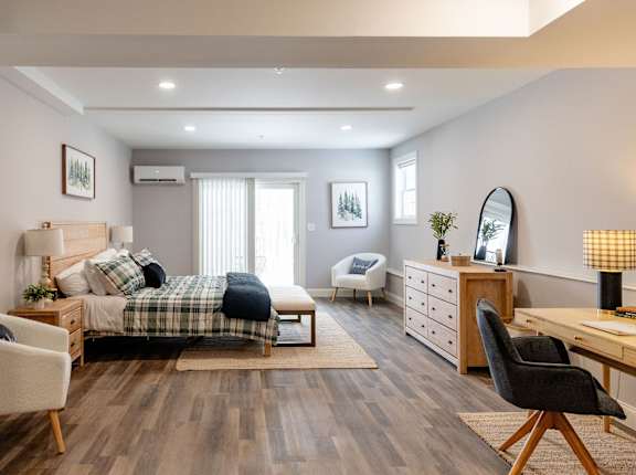 A well-lit bedroom with a bed, chair, and desk.