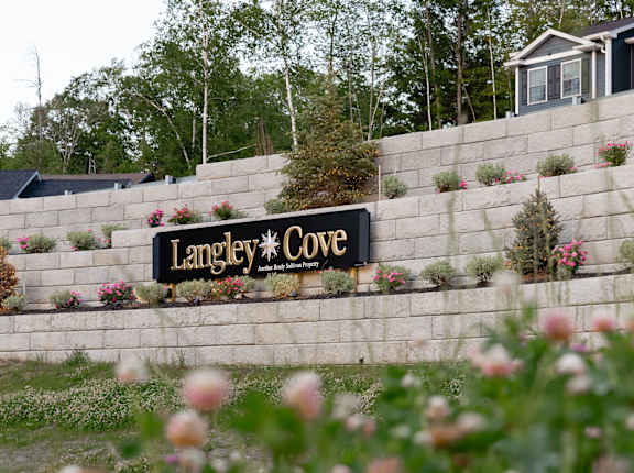 A sign that says "Langley Cove" is mounted on a wall with flowers in front.