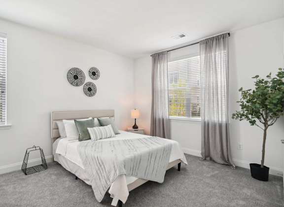 A bedroom with a bed, nightstand, and a plant.