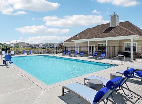 A pool with blue chairs and a house in the background.