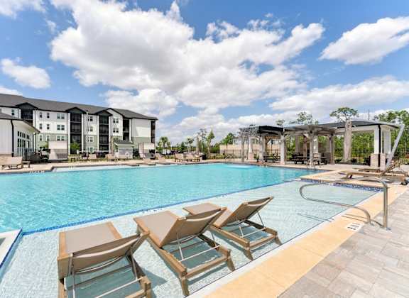 A pool with chairs and a building in the background at The Hendry Apartments, Fort Myers, FL, 33905