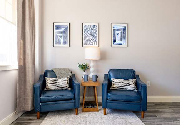 Two blue chairs with pillows and a small table between them.