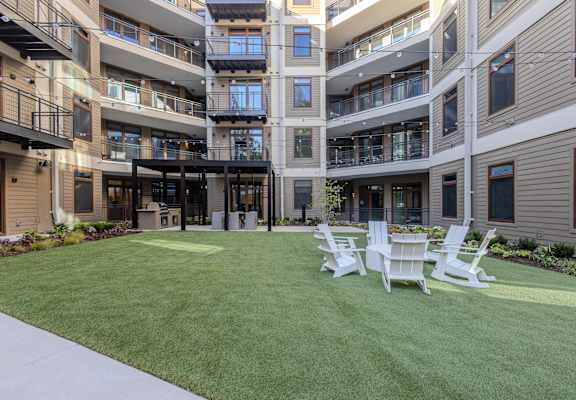 A large grassy area with four white chairs in front of apartment buildings.