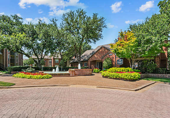 a fountain sits in front of a brick building with trees in the background