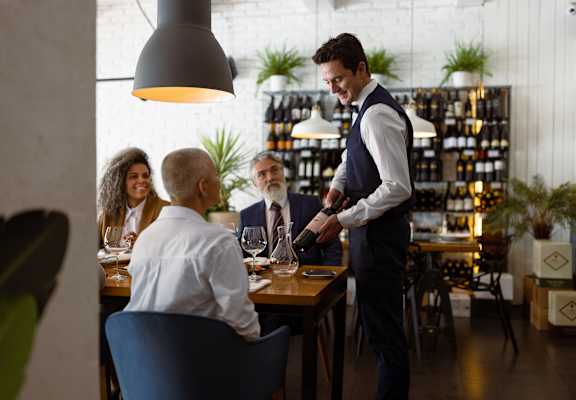 a waiter pouring a glass of wine for a group of people sitting at a table at Madison at Eden Brook, Columbia, MD, 21046