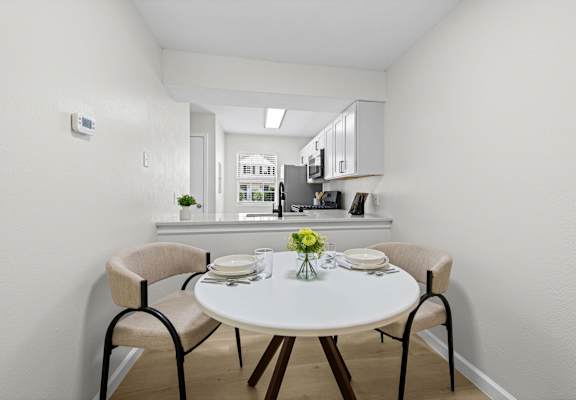 A white dining table with four chairs and a vase of flowers on top.