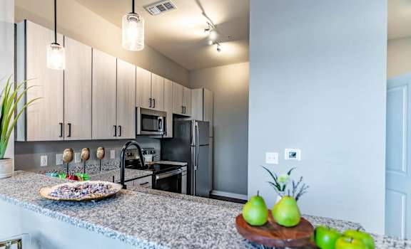 A kitchen with granite countertops and a tray of green apples.