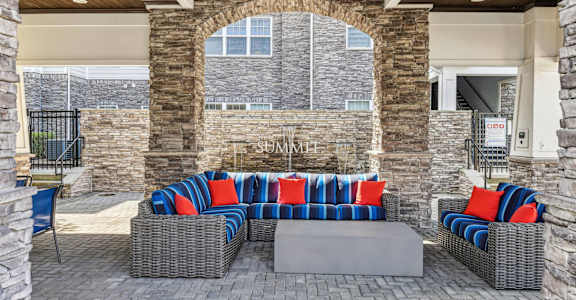A patio with a grey wicker couch and a stone wall.