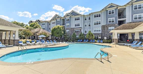 A large swimming pool surrounded by apartment buildings and lounge chairs.