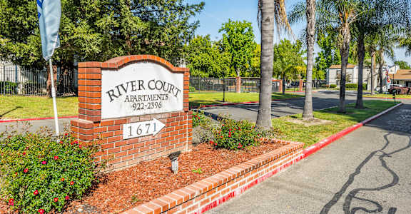 A sign for River Court Apartments is displayed in front of a building.