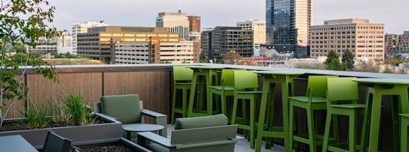 A rooftop patio with green chairs and tables overlooking a city skyline.