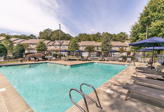 a swimming pool with chairs and umbrellas at the enclave at woodbury apartments
