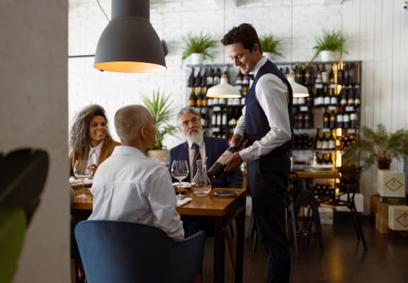 a waiter pouring a glass of wine for a group of people sitting at a table in a