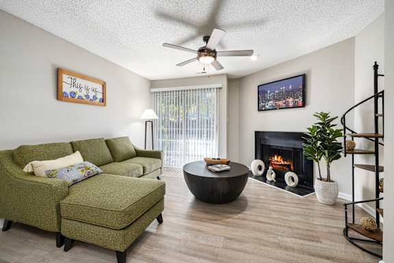 A living room with a green couch, a fireplace, and a TV on the wall.