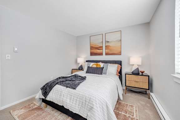 A bedroom with a bed, nightstands, and pictures on the wall.