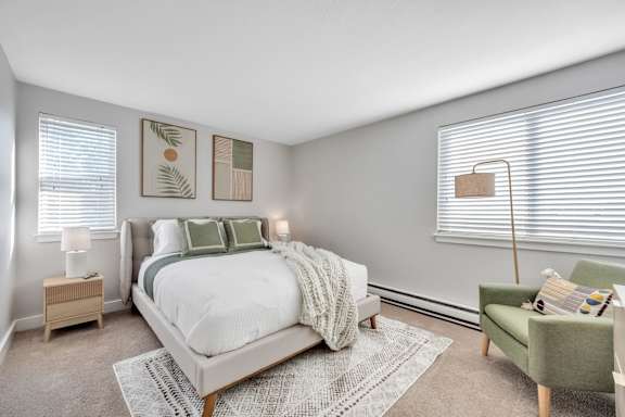 A bedroom with a large bed, a green chair, and two lamps.