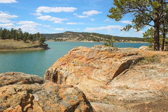 A tree stands on a rocky outcrop by a lake.