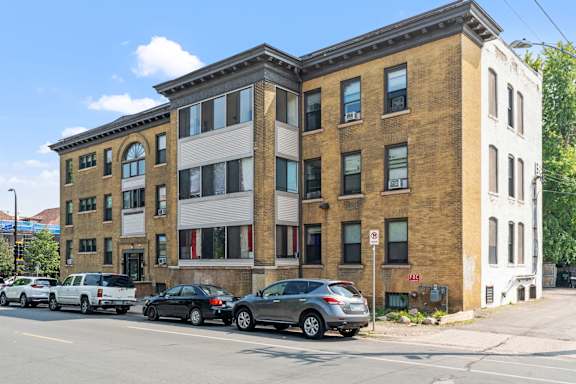 A building with a mix of brick and white siding has cars parked in front.