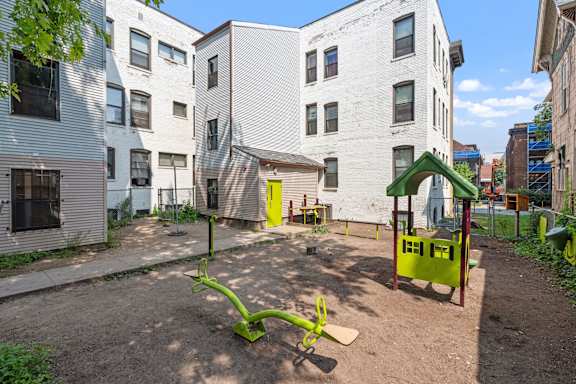 A playground with a green slide and a yellow slide in the middle of a dirt area.