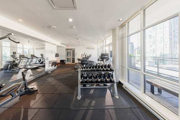 a gym with cardio equipment and large windows