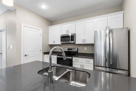 an empty kitchen with stainless steel appliances and white cabinets