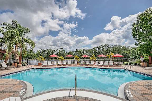 A large outdoor swimming pool surrounded by red umbrellas and lounge chairs. at Northlake Park Apartments, Orlando, 32827
