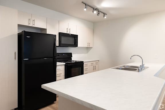 A black refrigerator and microwave in a kitchen with white countertops.