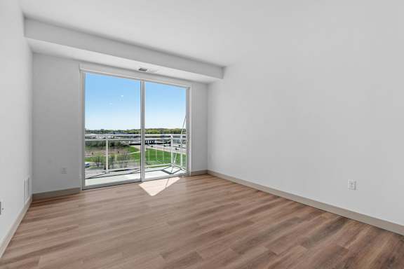 an empty living room with a sliding glass door to a balcony at The Mera, St Louis Park, 55426
