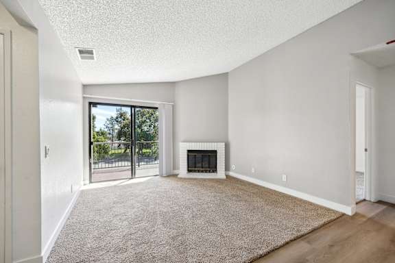 an empty living room with a fireplace and a door to a balcony