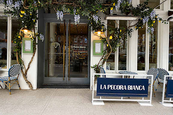 A sign that says La Pecora Bianca sits in front of a doorway.