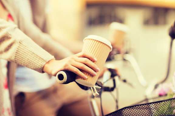 A person is holding a cup of coffee while riding a bicycle.at Slate Yard Apartments, Salford, M3 5EX