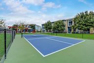 A tennis court is surrounded by a black fence and a building is in the background.