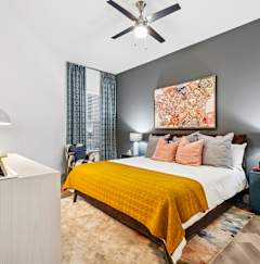 A bedroom with a bed, a lamp, a painting, and a ceiling fan.