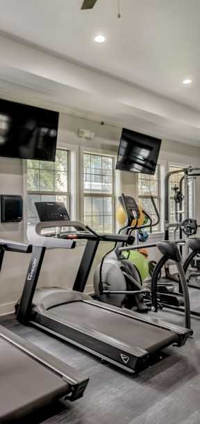 A spacious gym with treadmills, elliptical machines, and a fan.