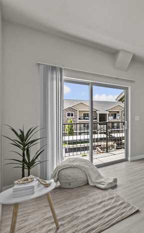 A room with a white door, a table with a plant, and a window with a view of a building outside.