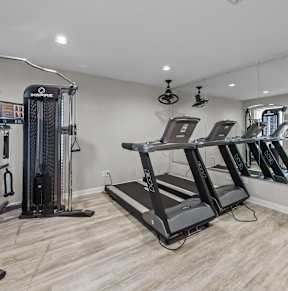A spacious home gym with a variety of equipment including treadmills, a weight machine, and a rowing machine.