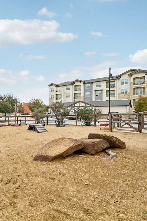 A sandy area with a large rock in the middle and a horse in the background.