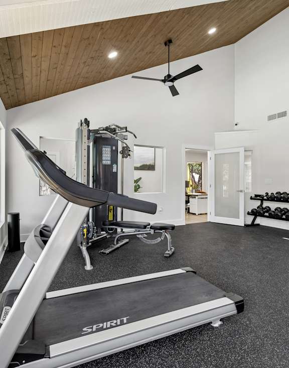 A gym with a treadmill, weights, and a fan.