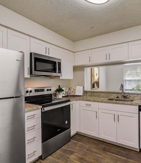 A kitchen with a refrigerator, microwave, oven, and sink.